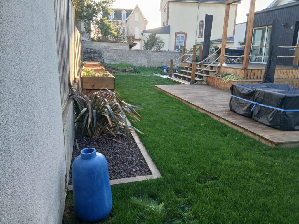 Jardin aménagé avec pelouse, massifs et terrasse en bois par Les Jardins du Val de Vire