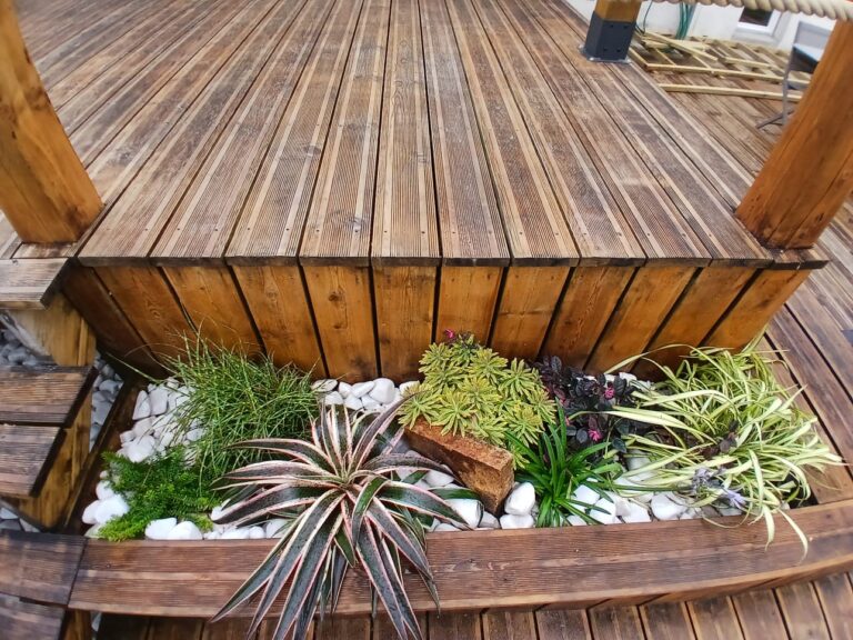 Terrasse en bois avec massif de plantes et galets blancs par Les Jardins du Val de Vire