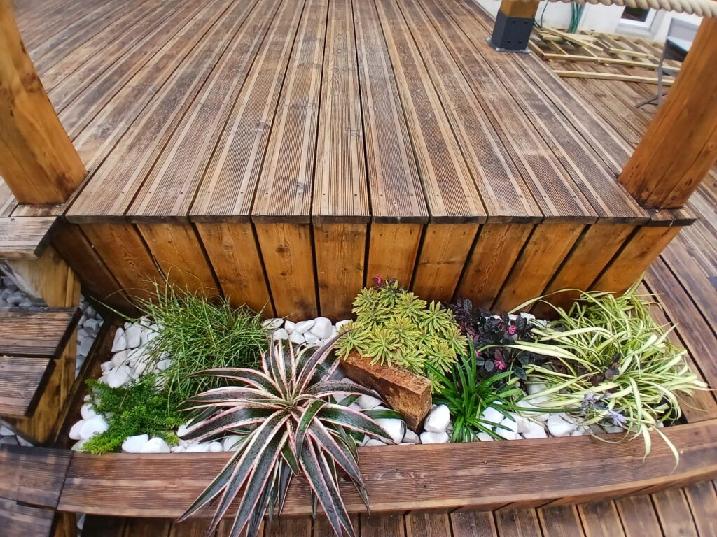 Terrasse en bois avec massif de plantes et galets blancs aménagé par Les Jardins du Val de Vire